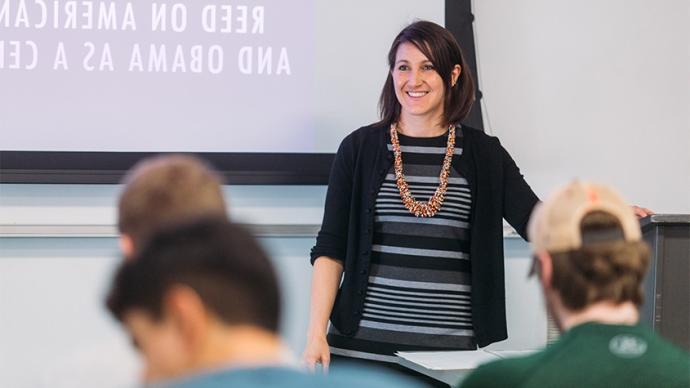 Professor presenting to students in front of a screen.