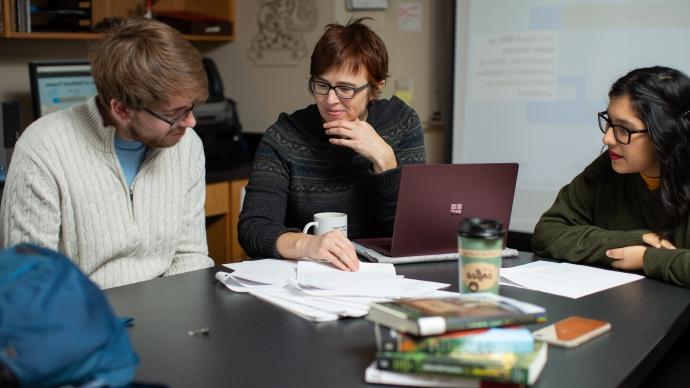 amy stone sits at table with a female student and a male student, all studying papers related to her research