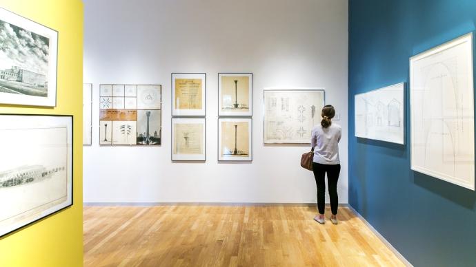 A woman reflects on an O'Neil Ford rendering on a white and blue wall