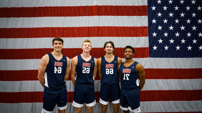 卡莱布·詹金斯22岁, 坦纳·布朗，23岁, AJ Clark’21, and Ben Hanley '21 smile wearing Team USA uniforms in front of an american flag