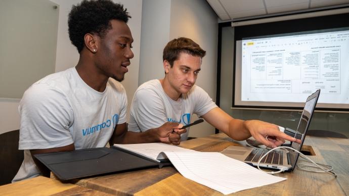 Michael Marquez and Jalen White point at a computer screen with screenshots of the Commuv app