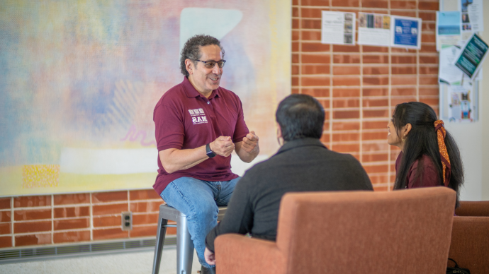 Juan Sepulveda sits in front of two students, talking to them 