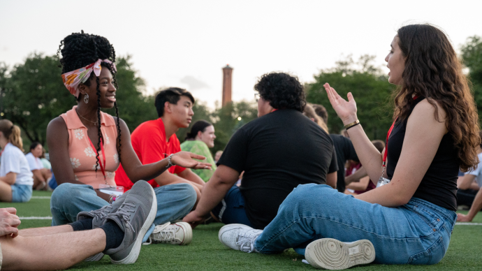 学生 from the Class of 2026 sit in a field and chat at Tiger Takeoff 2022 with the Murchison Tower on the horizon