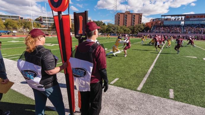 Dennis Ugolini and Jennifer Steele watch a 澳门金沙线上赌博官网 Football game from the sidelines with the down and distance markers