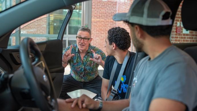 Professor leans in front of open vehicle door with two 学生 inside car