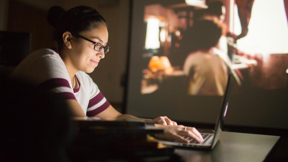 Woman typing on computer as movie plays in the background