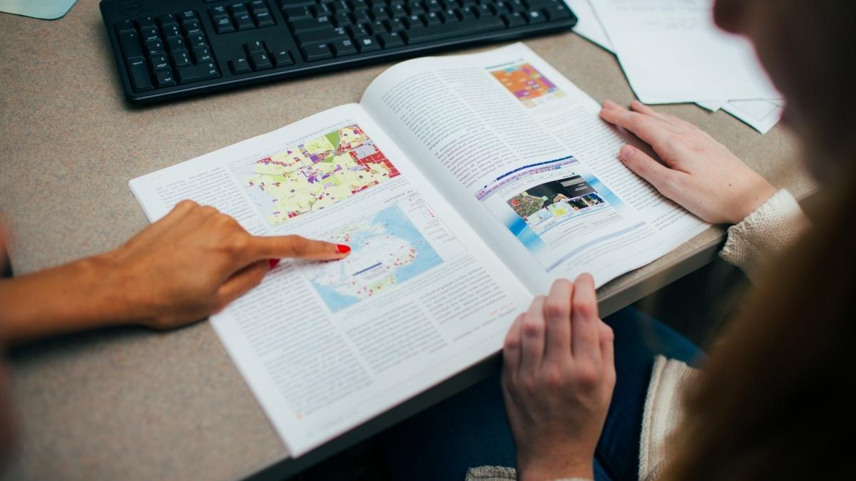 One student pointing to a diagram in a book while another student looks on