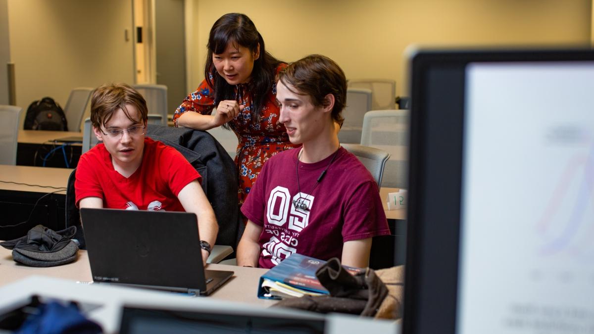 Hoa Nguyen and two students work at a laptop discussing math modeling.