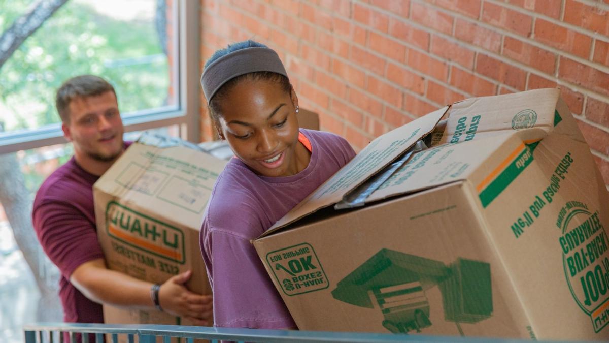 Two students carrying big boxes on move-in day up a stairway to their dorms