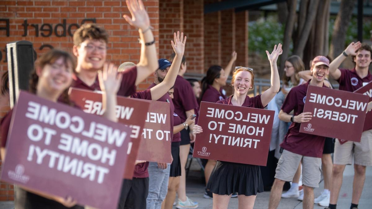 Students holding welcome signs, smiling and waving